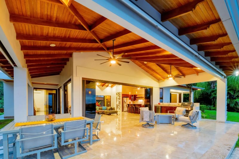 Casa Hacienda Jaguar · 36. A covered outdoor terrace with a wooden beamed ceiling and tiled floor provides an outdoor dining area, a barbecue grill, and lounge seating, connecting to the villa's interior and surrounded by jungle.
