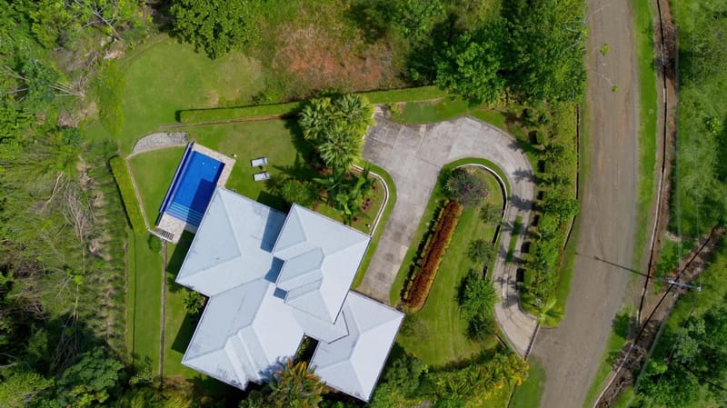 Casa Hacienda Jaguar · 42. An aerial view reveals the villa's multi-roofline design, a bright blue swimming pool, and a winding paved driveway, all surrounded by lush green lawns and dense tropical jungle.