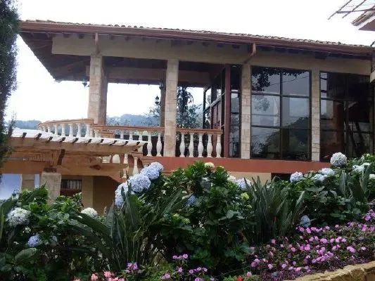 A covered veranda with large windows overlooks a garden of flowering plants.