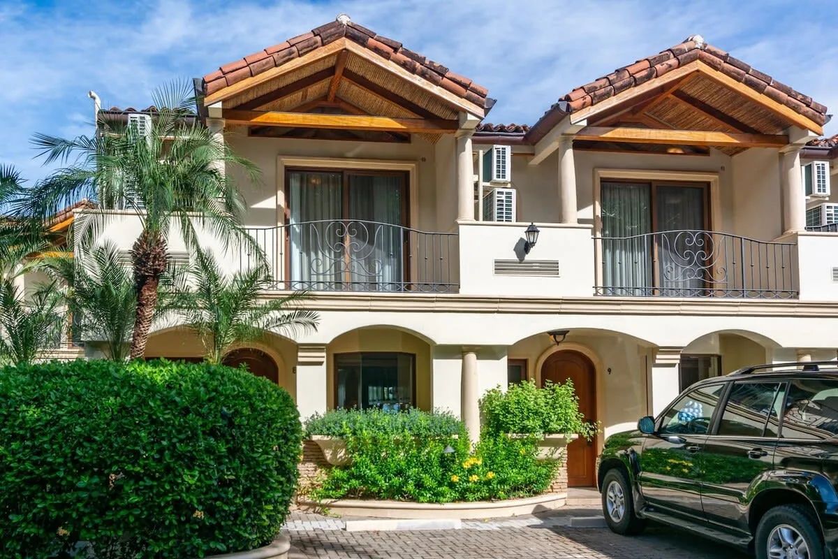 A two-story residential building with balconies, arched entrances, and landscaping.