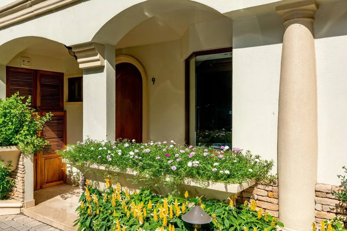 A sunlit building entrance with arched openings and flowering plants.