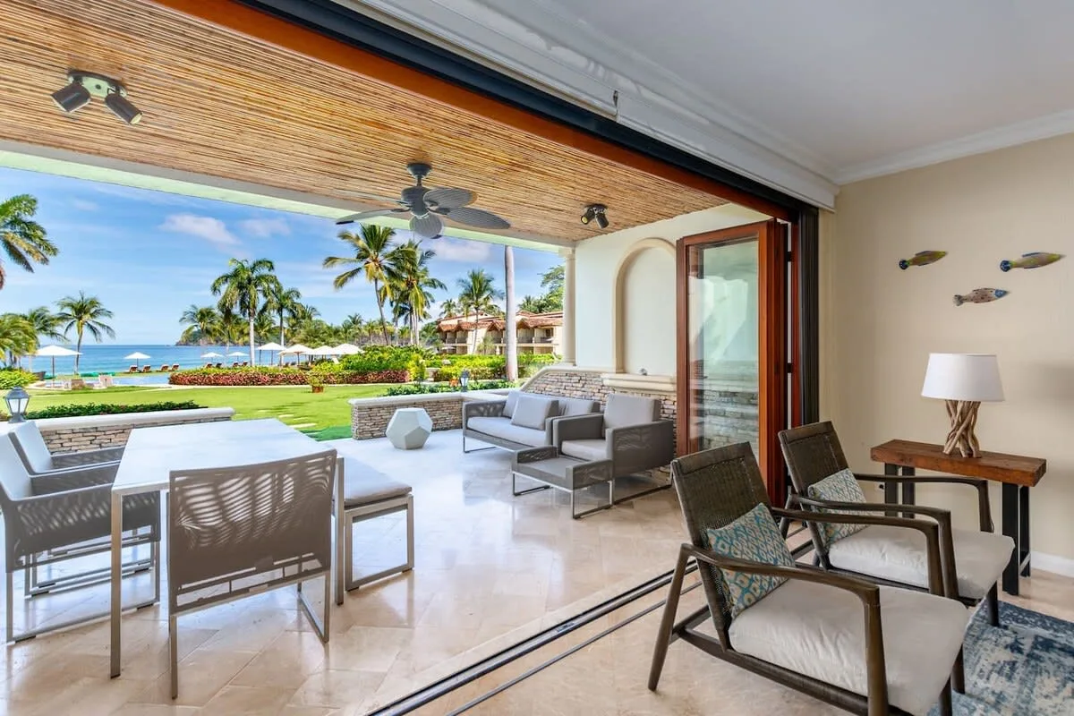A furnished patio opens onto a garden with palm trees and a view of the ocean.
