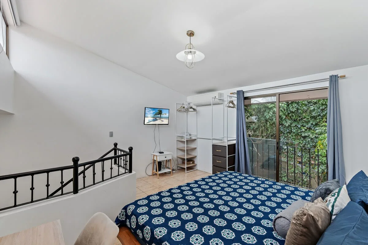 A bedroom with a patterned bed, open clothing shelves, and glass doors opening to a balcony.
