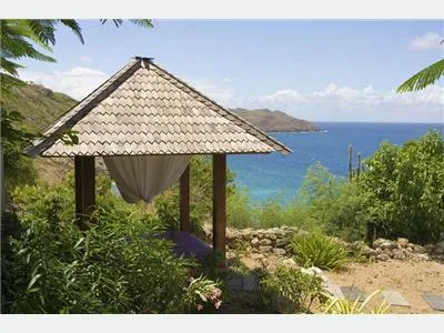 Un refugio al aire libre con sombra ofrece vistas al mar azul y las colinas verdes.
