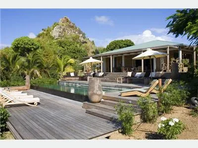 Una piscina exterior y una terraza están junto a un edificio moderno, con una colina rocosa detrás.