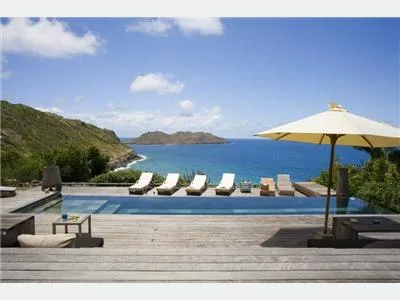 Una terraza con piscina al aire libre mira a una bahía, con tumbonas y una sombrilla.