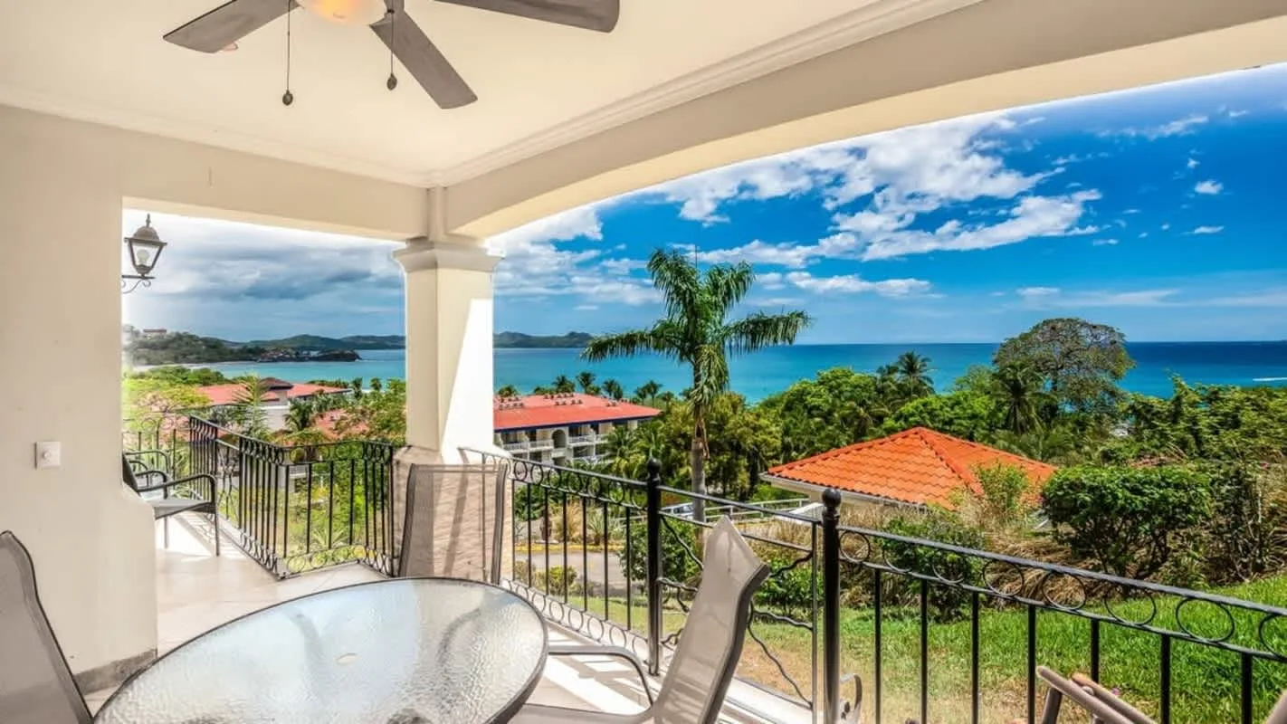 A covered balcony overlooks tropical greenery and the ocean.