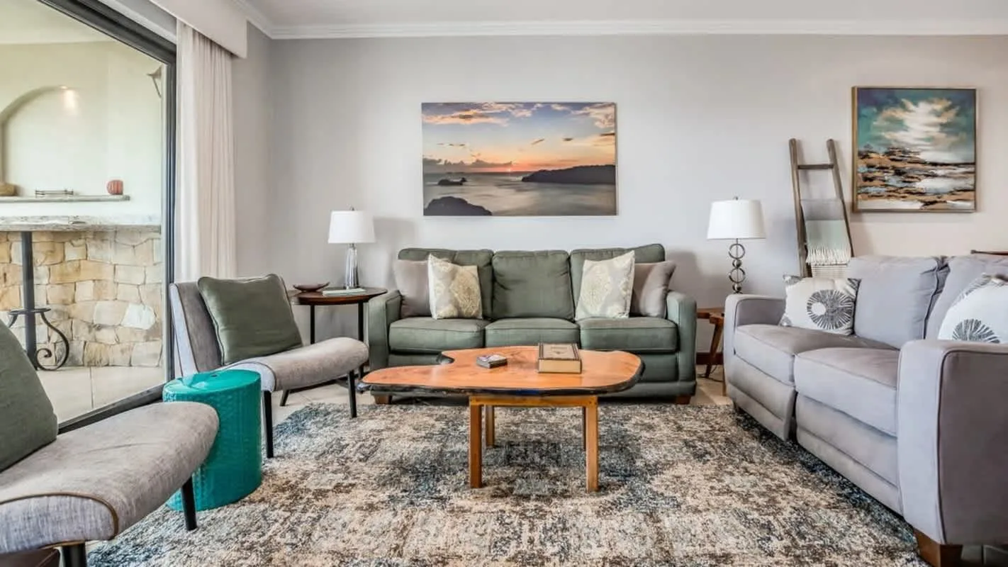 A living room with seating around a wooden coffee table and coastal artwork.