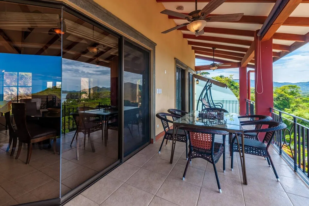 A covered outdoor dining area with a table and seating beside sliding glass doors.