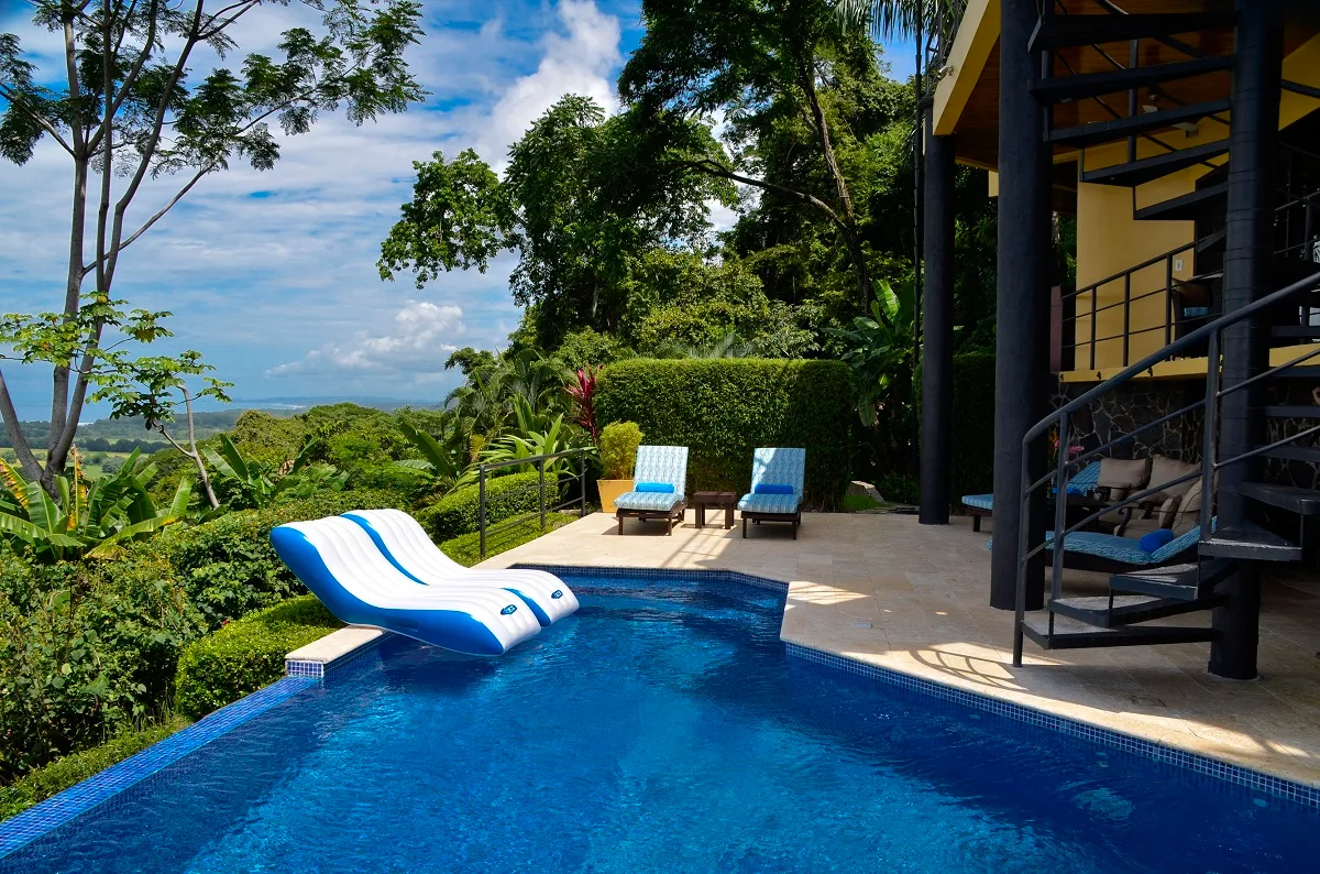 A swimming pool sits beside a terrace with loungers and tropical greenery.