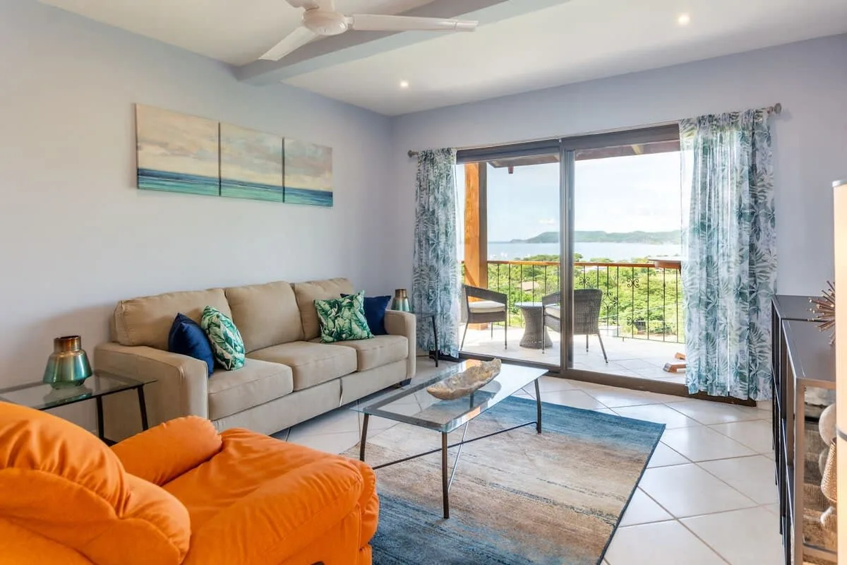 A bright living room with seating and glass doors opening onto a balcony.