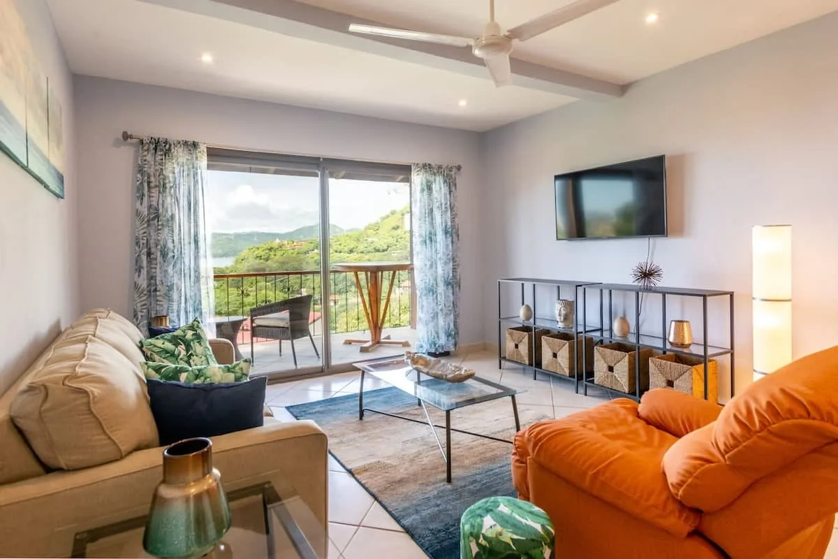 A bright living room with seating, a television, and sliding glass doors opening to a balcony.