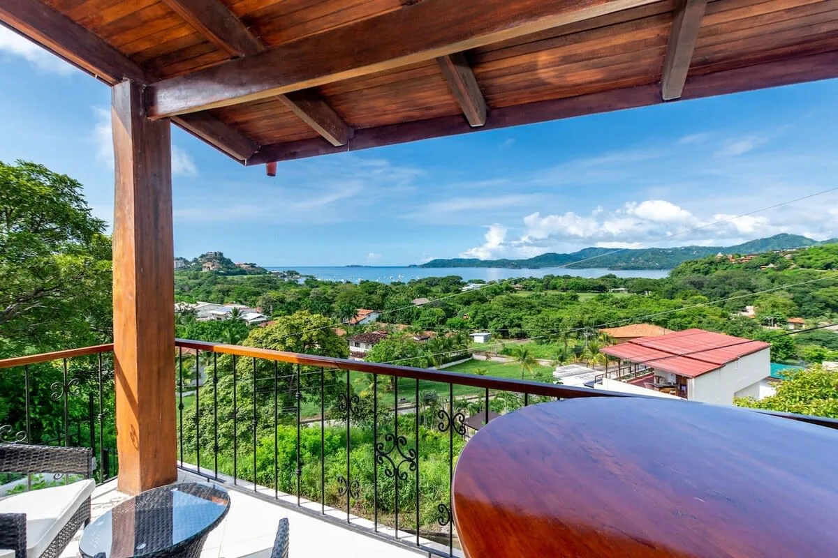 A covered balcony overlooks green hills and a distant body of water.