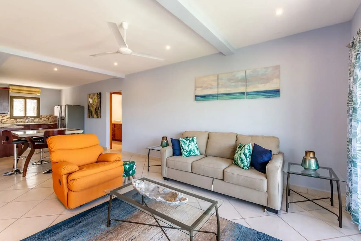 A living room with seating, a glass coffee table, and an open kitchen area.
