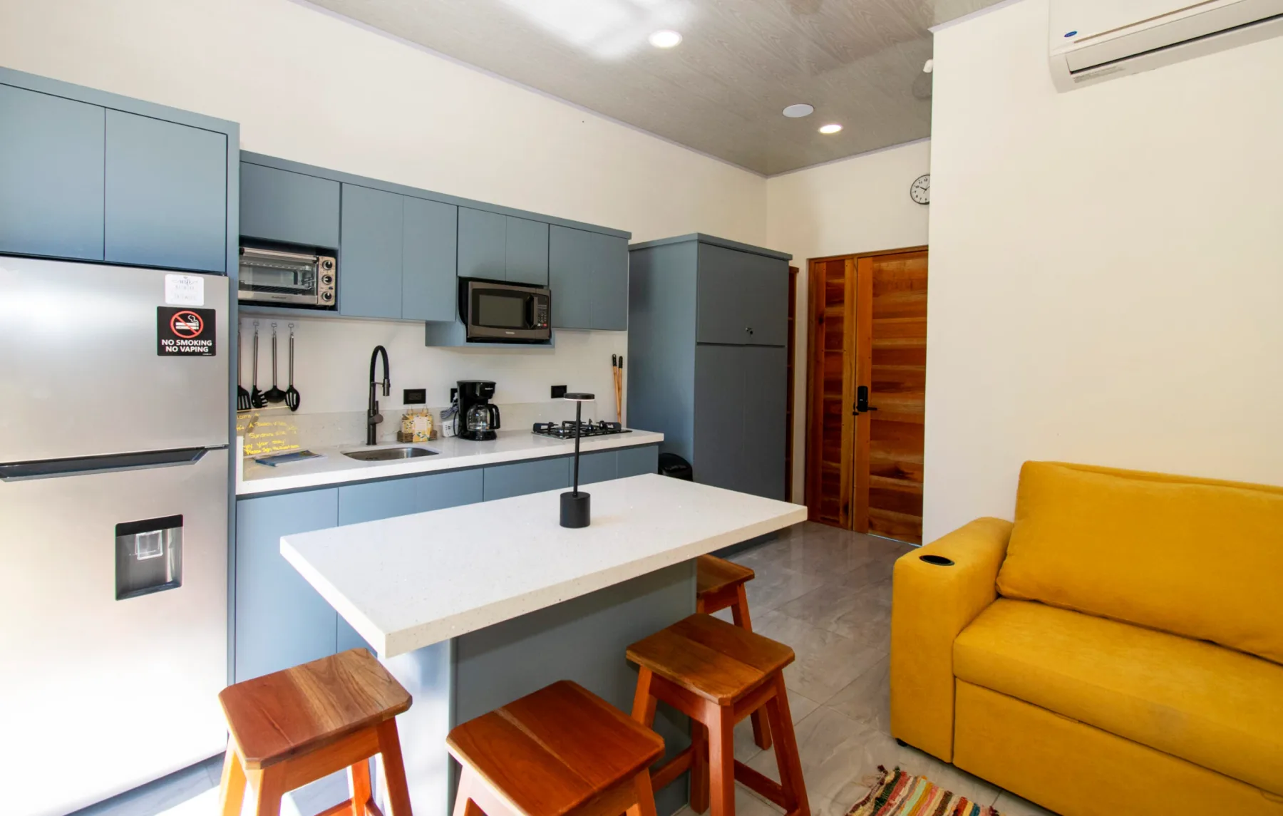 Una cocina compacta y sala de estar con gabinetes azules, una isla blanca y asientos amarillos.