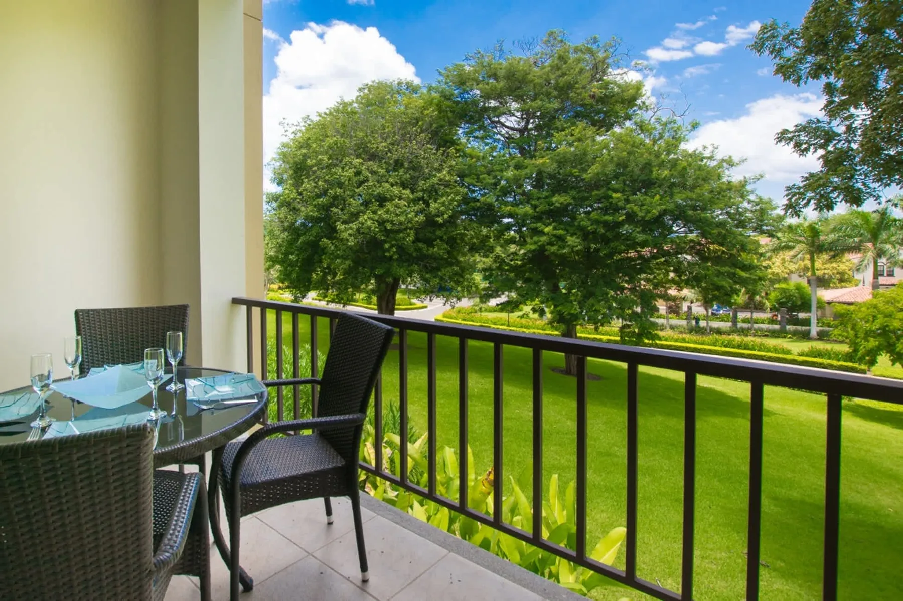 A balcony with outdoor seating overlooks a green lawn and trees.