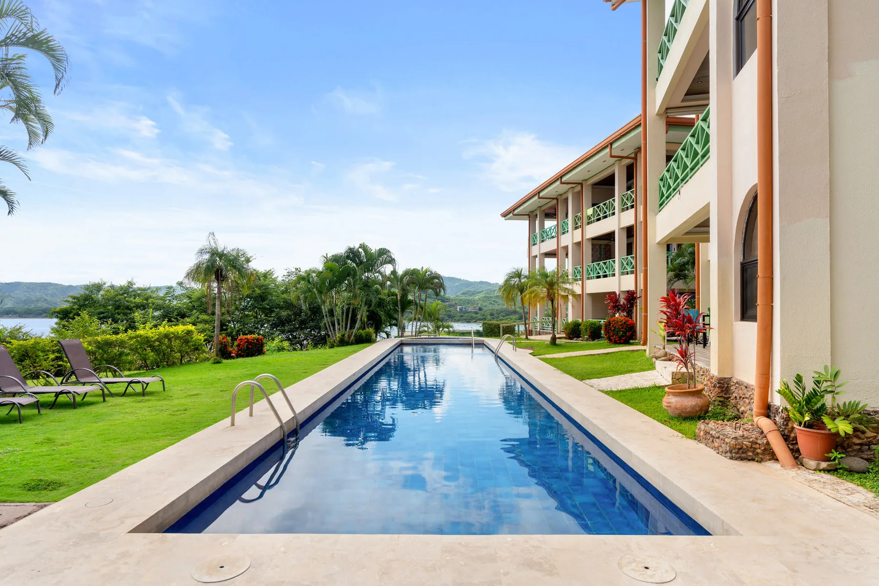 A swimming pool beside a landscaped lawn and a multi-story building.