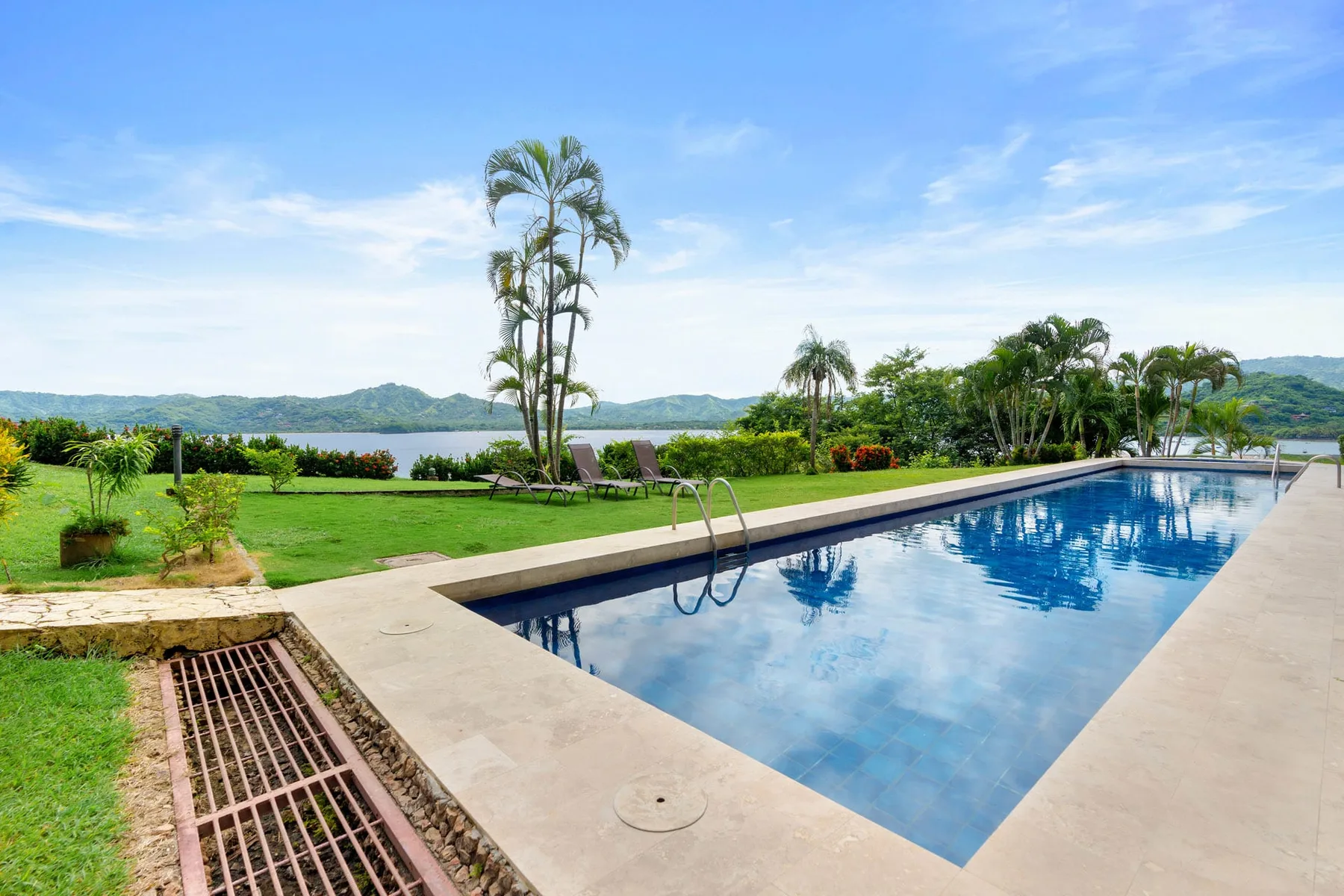 An outdoor swimming pool overlooks a landscaped garden and distant hills.