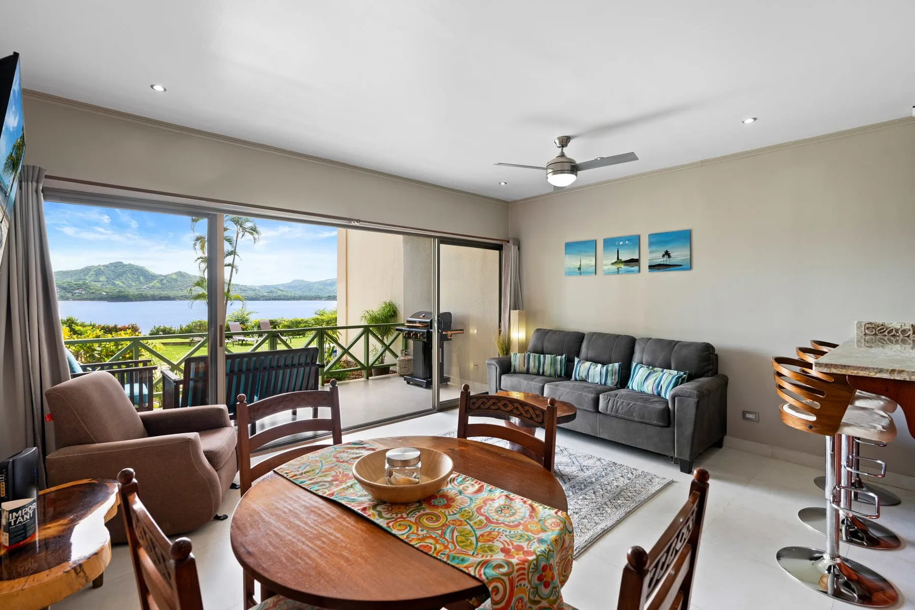 A living and dining area opens onto a balcony overlooking a green landscape.
