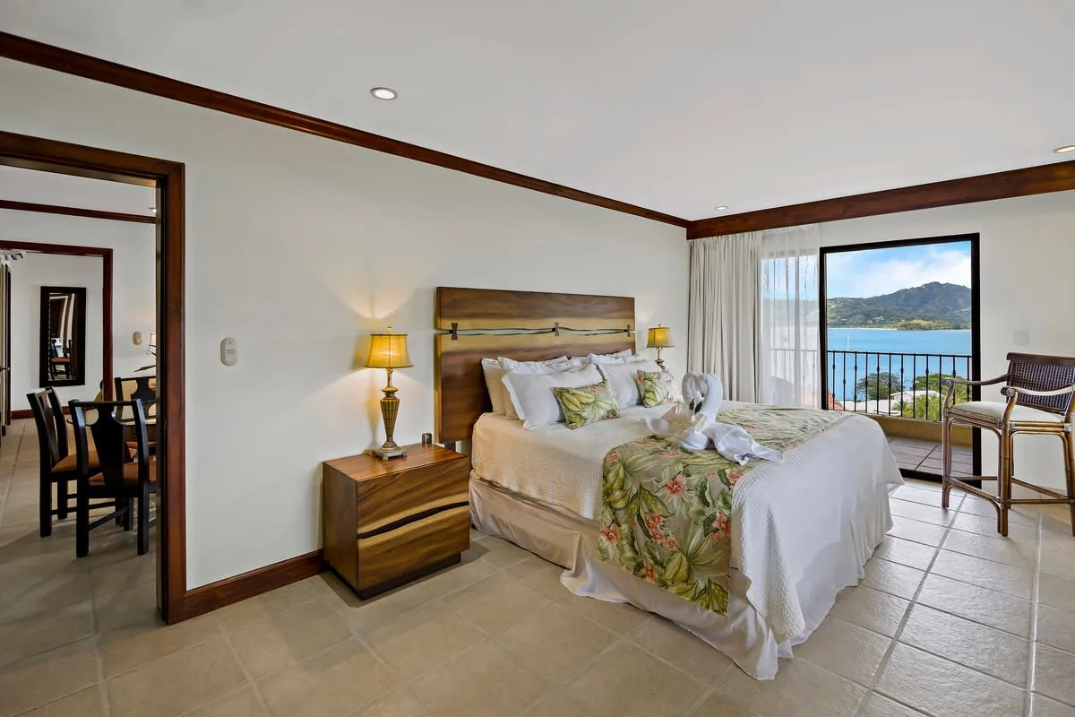 A bedroom with a bed, bedside table, and balcony doors overlooking the water.