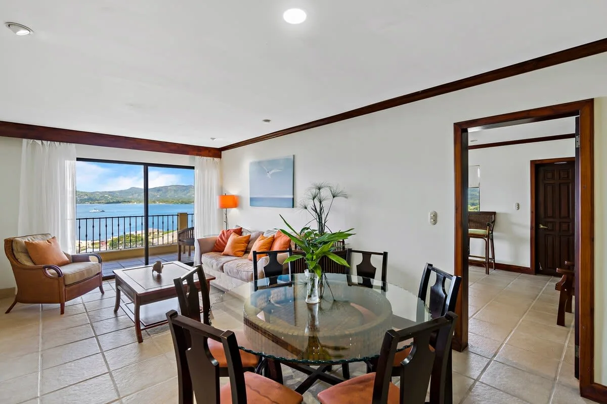 A bright living and dining area opens onto a balcony with a water view.