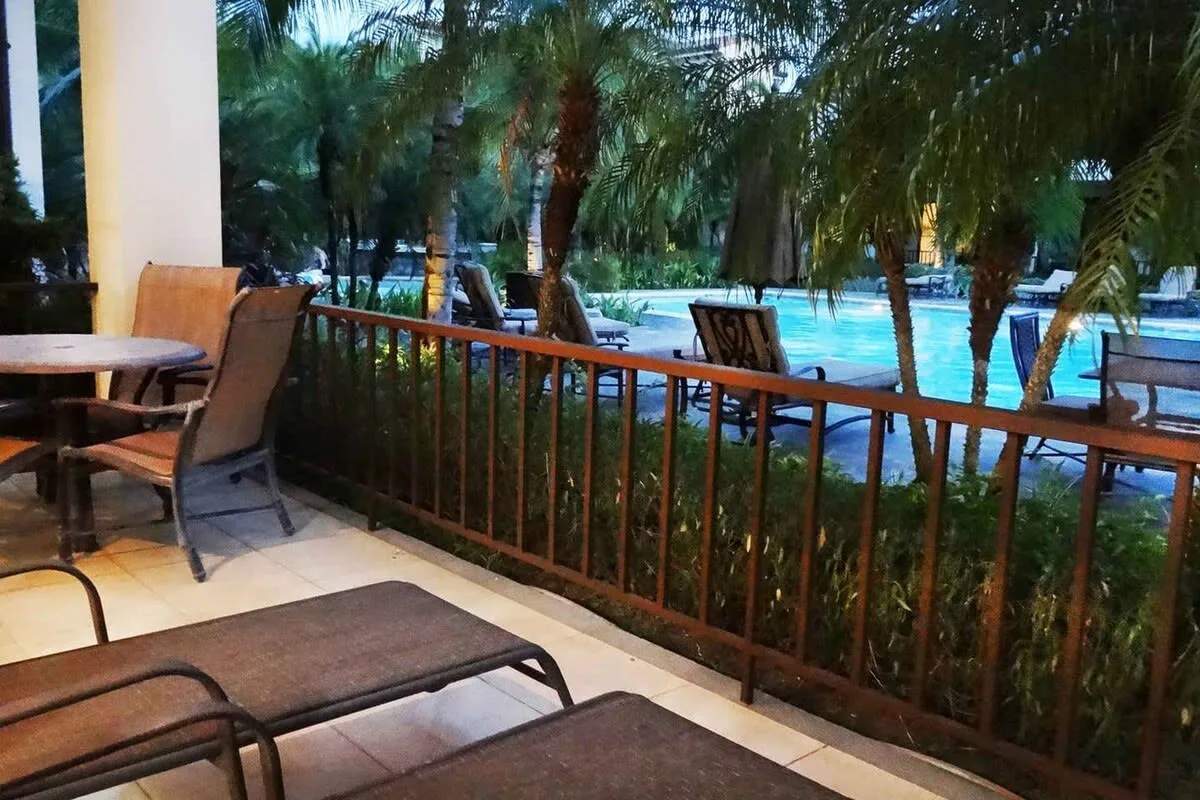 Un patio cubierto con asientos da a una piscina rodeada de palmeras.