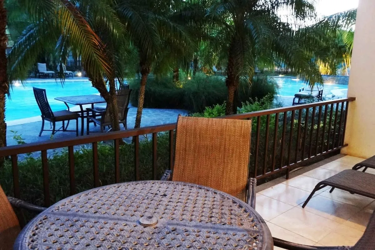 Un patio de baldosas da a una piscina, con asientos al aire libre y palmeras.