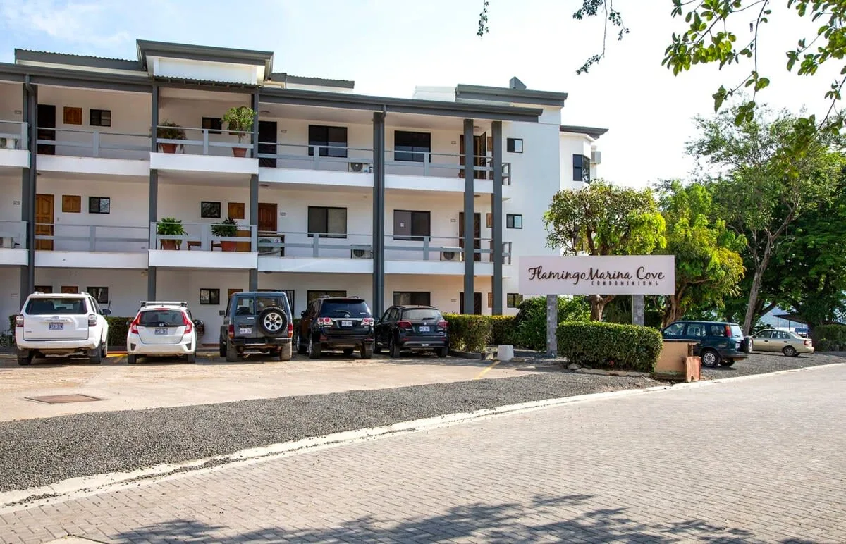 A multi-story residential building stands beside a paved parking area.