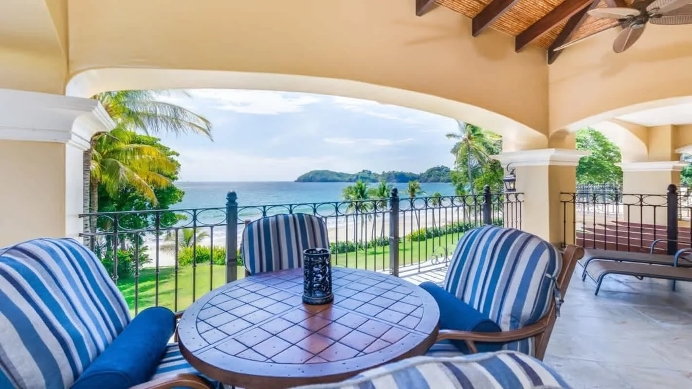 A covered terrace overlooks the ocean, with striped seating around a round table.
