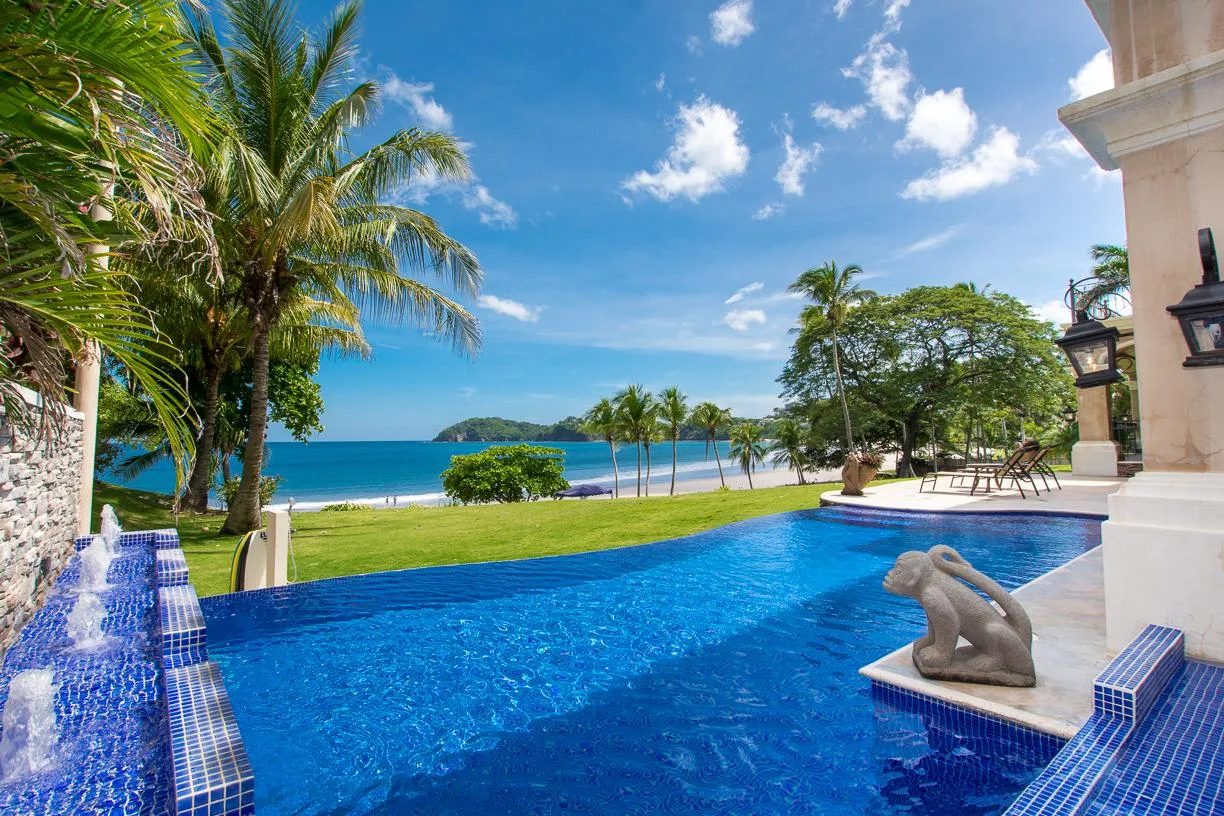 Una piscina al aire libre da a un césped, palmeras y el mar.