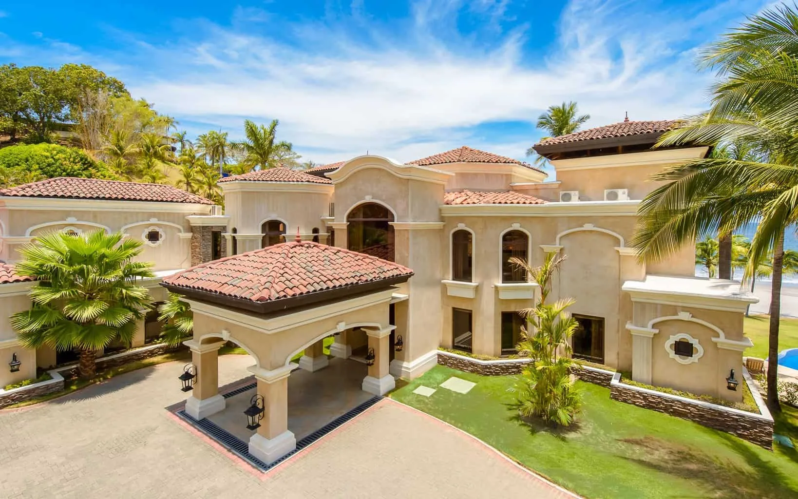 Una villa grande con techo de tejas está rodeada de palmeras y jardines.