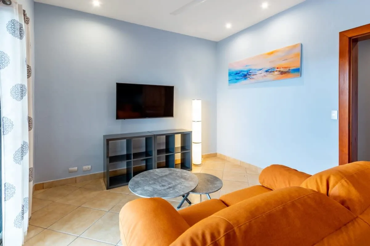 A living room with orange seating, a television, and wall art.