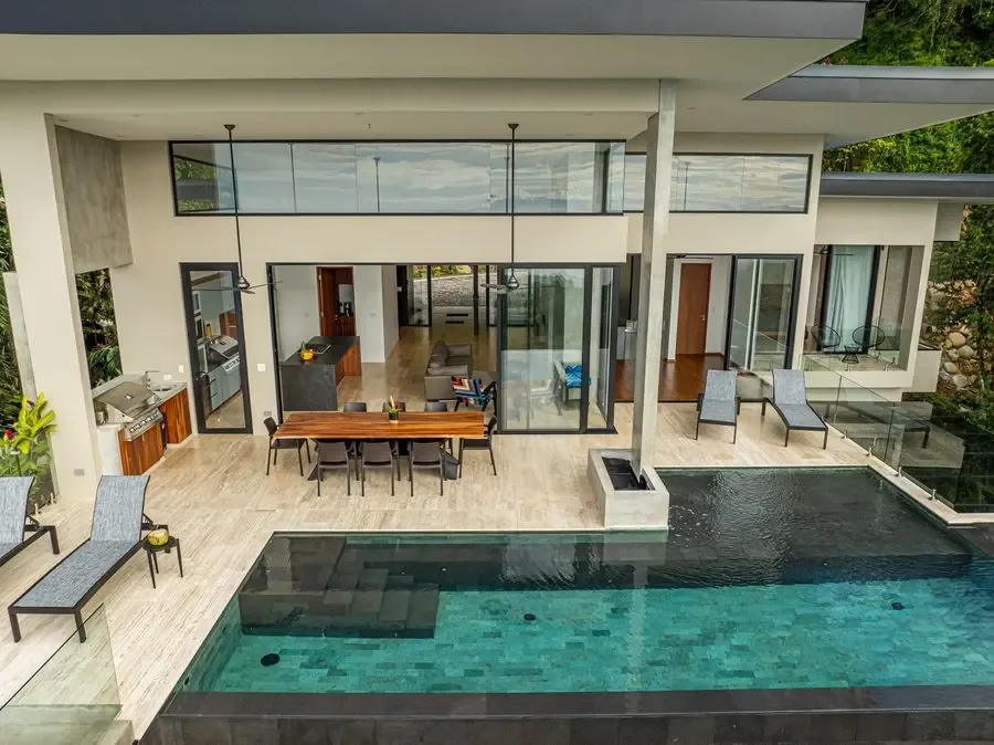 Una casa moderna da a un patio con piscina y asientos al aire libre.