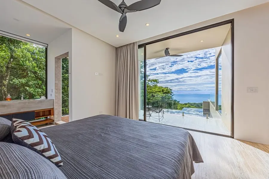 Un dormitorio con una cama frente a una amplia abertura acristalada y vistas al mar.