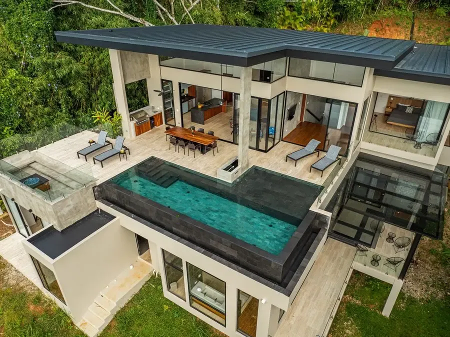 Una casa moderna con una piscina rectangular y asientos en el patio.