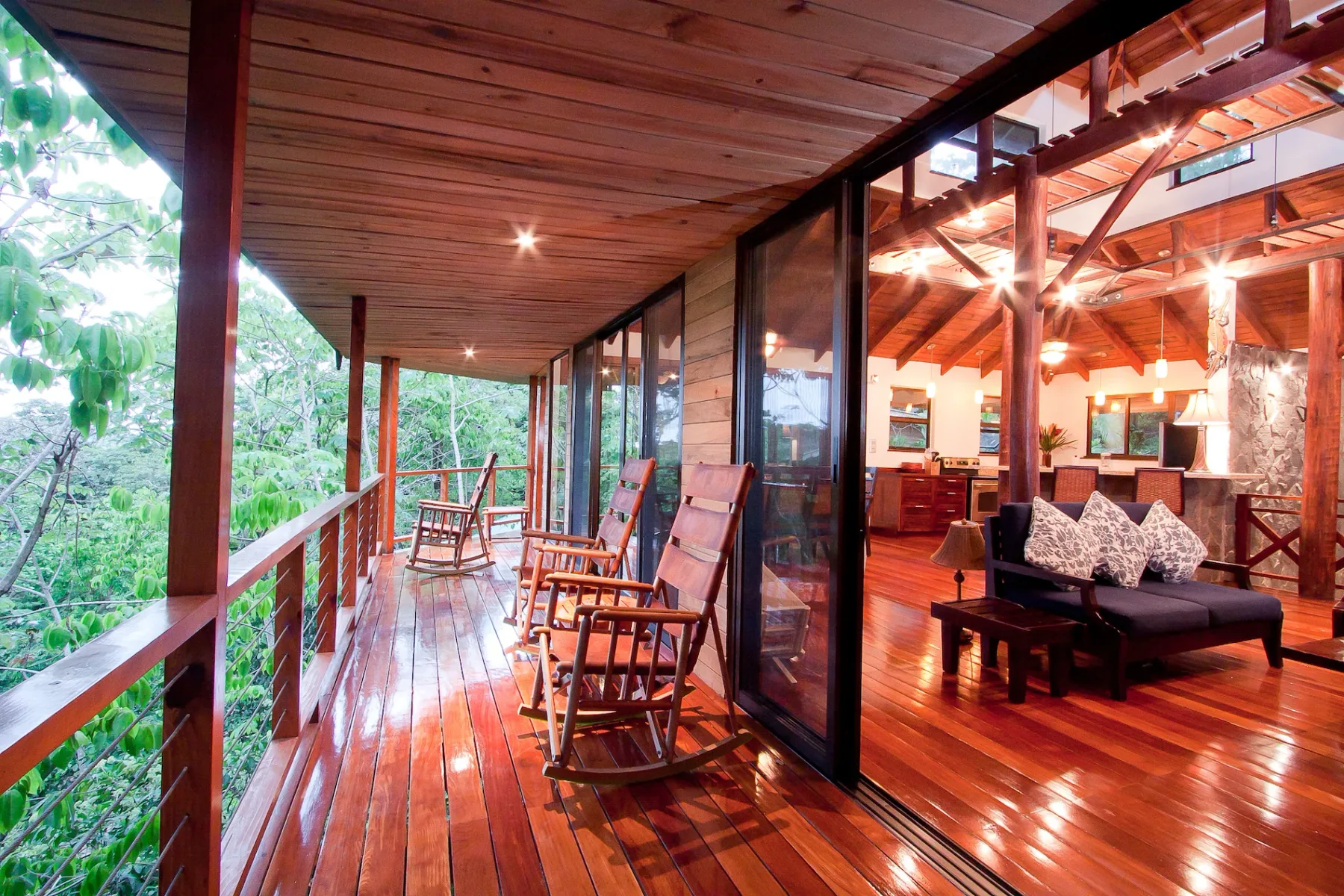 Bali Tree House · 13. A covered wooden terrace with rocking chairs overlooks trees and connects to an indoor living area through sliding glass doors.