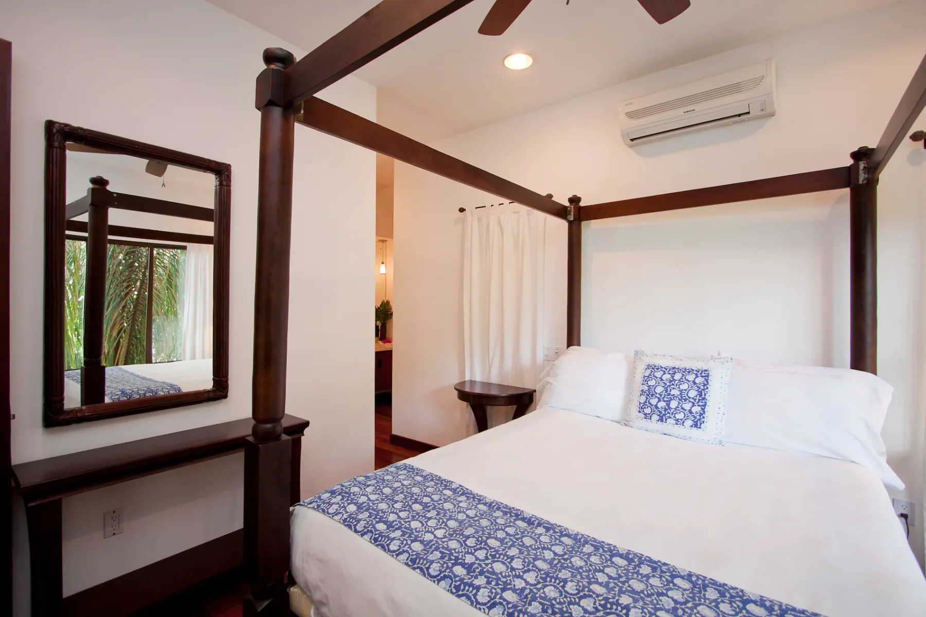 Bali Tree House · 23. A bedroom features a dark wood four-poster bed with white linens and blue patterned accents, a wall mirror, and an air conditioning unit.