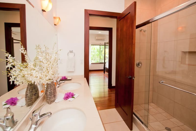 Bali Tree House · 29. A bathroom features a double vanity, a large mirror, and a tiled walk-in shower, with a view into an adjacent bedroom.