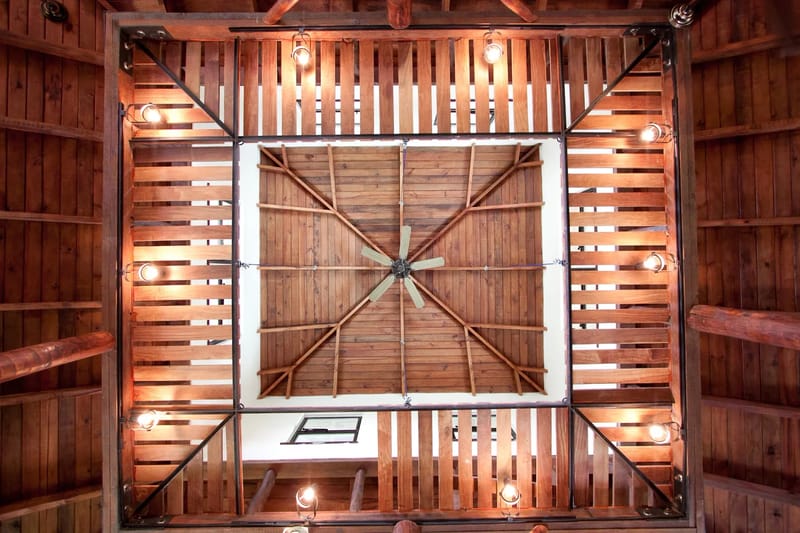 Bali Tree House · 15. A wooden ceiling structure with exposed beams, slatted sections, a central ceiling fan, and multiple mounted light fixtures.