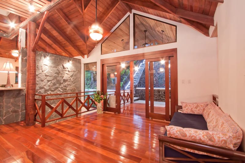 Bali Tree House · 9. A living room with a wooden vaulted ceiling, hardwood floor, stone accent wall, and a daybed, featuring glass doors opening to an exterior staircase.