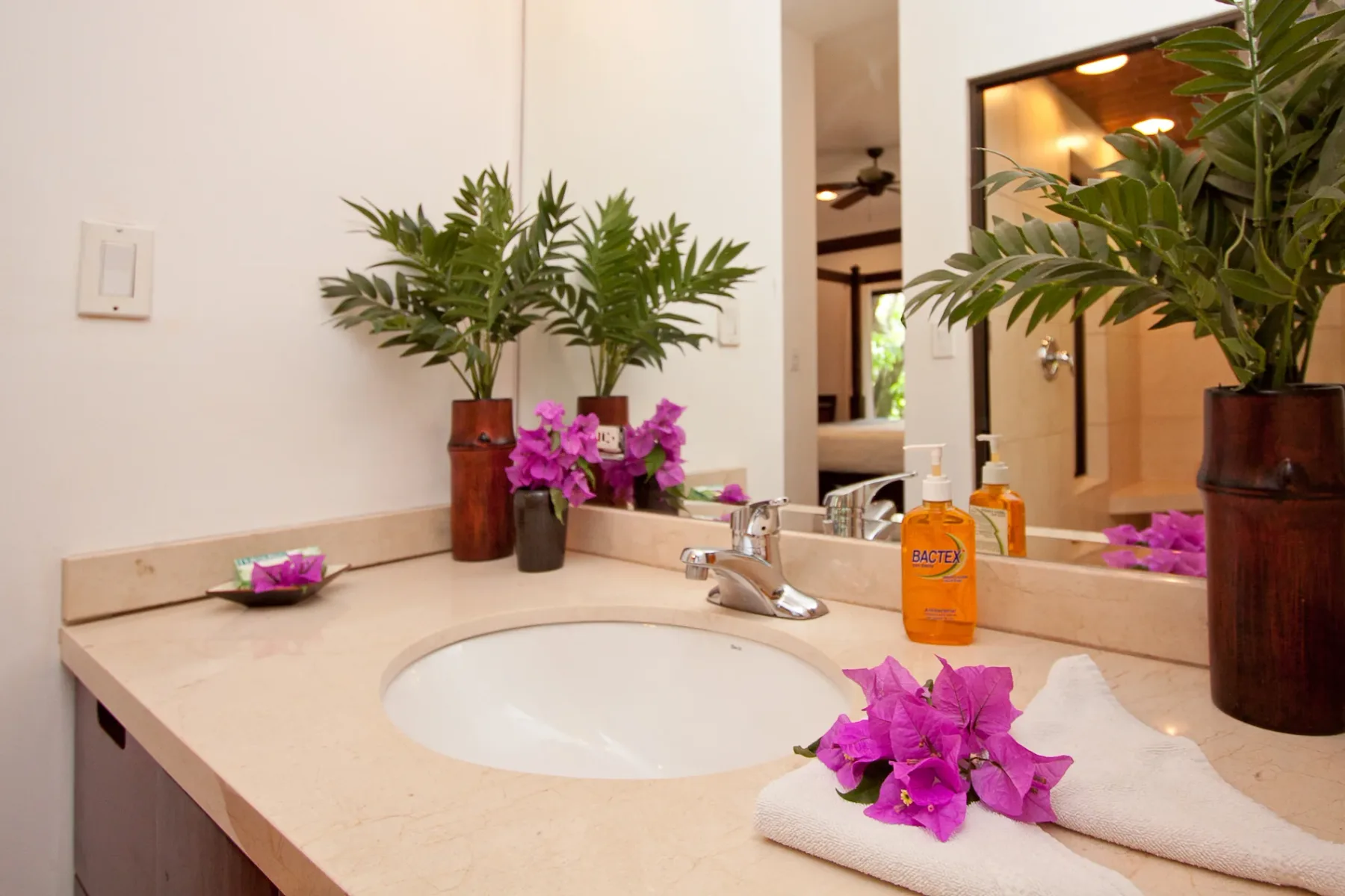 Bali Tree House · 25. A bathroom vanity features a single sink, chrome faucet, mirror, decorative plants, and towels. A bedroom is reflected in the mirror.