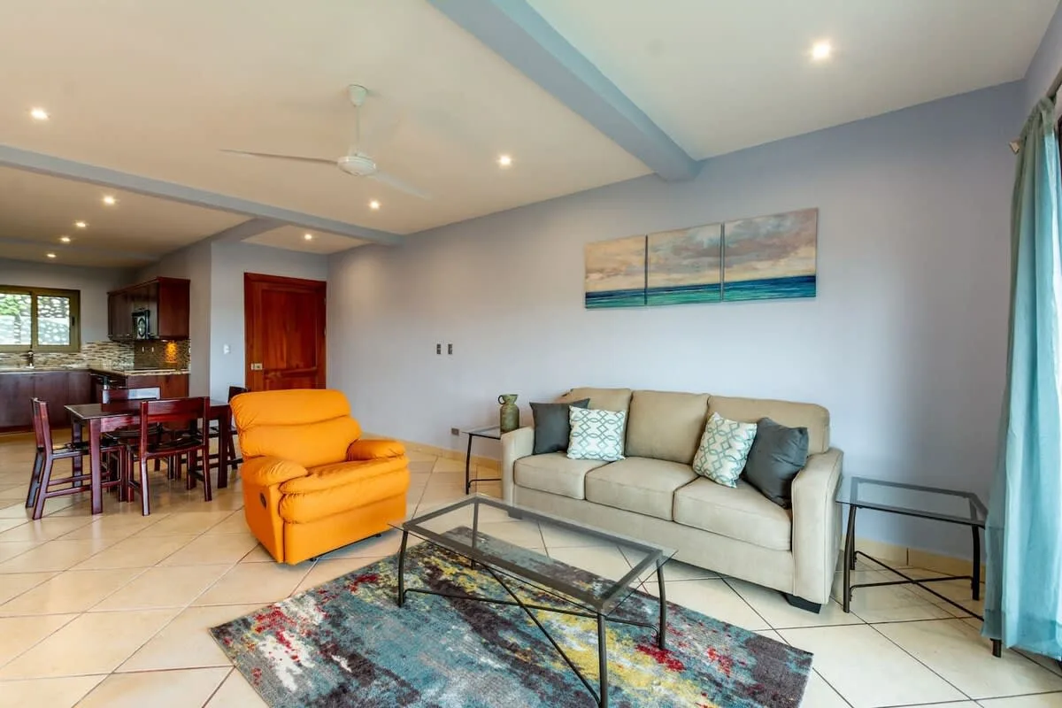 Una sala de estar con un sofá, un sillón naranja y una mesa de centro de vidrio.