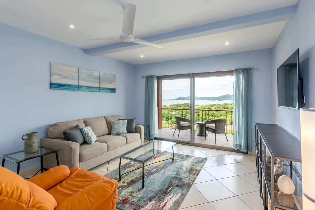 A living room with seating, a coffee table, and sliding glass doors opening to a balcony.