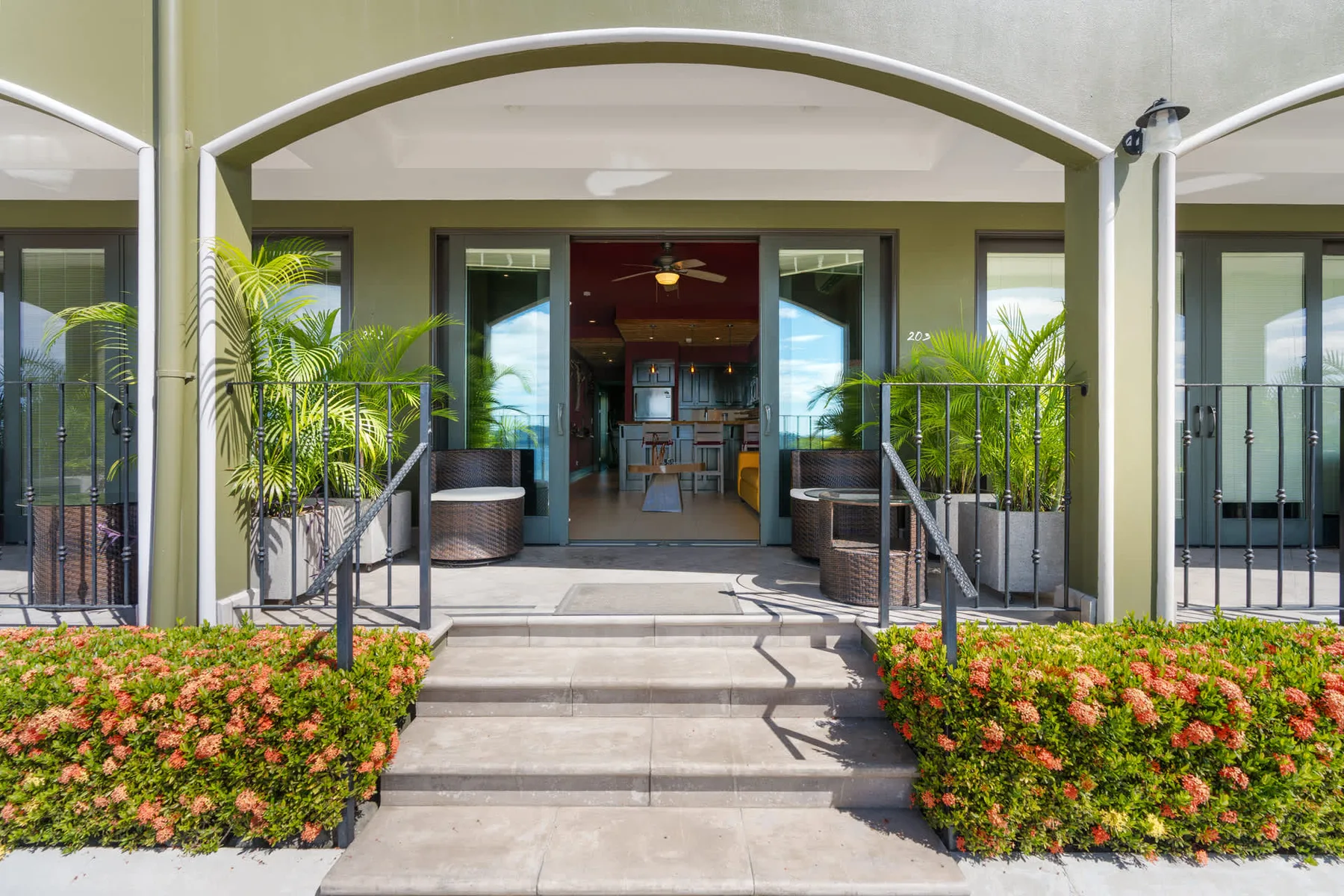 A covered patio with steps, seating, and potted plants faces an open glass doorway.