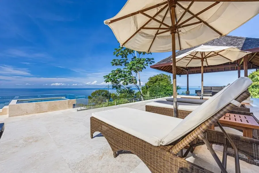 An outdoor terrace overlooks the sea, with cushioned seating beneath large umbrellas.