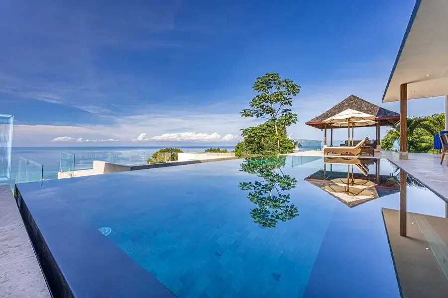An infinity pool overlooks the sea, with a shaded seating area beside it.