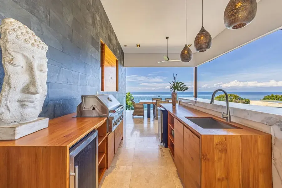 A modern kitchen with a long island and wide windows overlooking the ocean.
