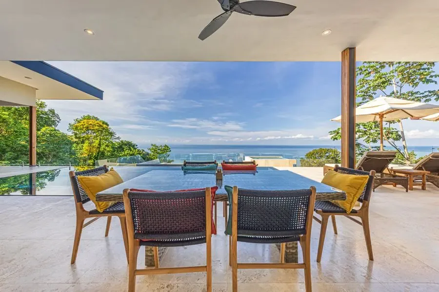 An outdoor dining area overlooks a swimming pool and the ocean.
