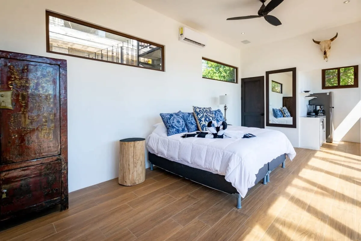 A bright bedroom with a bed, patterned pillows, and a ceiling fan.