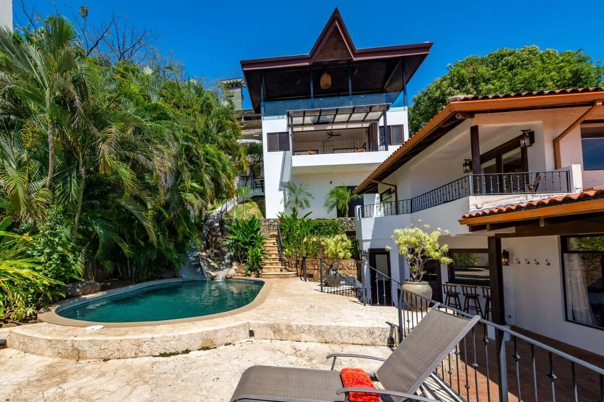 An outdoor pool beside a multi-level building, with lounge seating on the terrace.